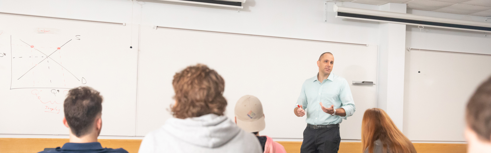 a man standing in front of a whiteboard with a group of people sitting in chairs