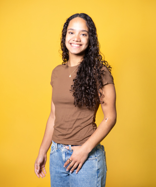 a woman with long curly hair wearing a brown shirt and blue jeans