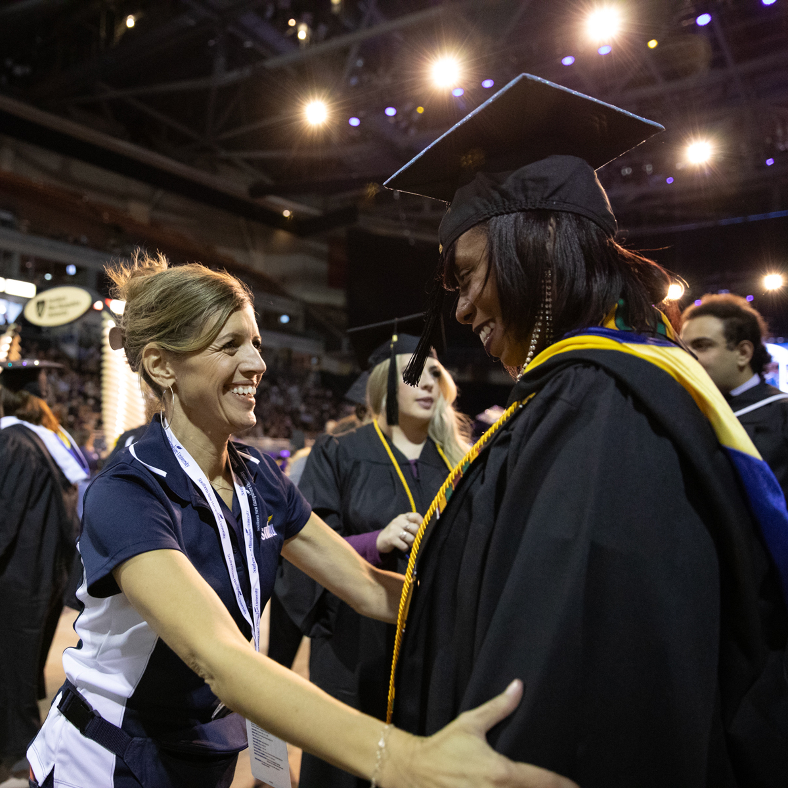 a woman in a graduation cap and gown shaking hands with a woman in a stadium