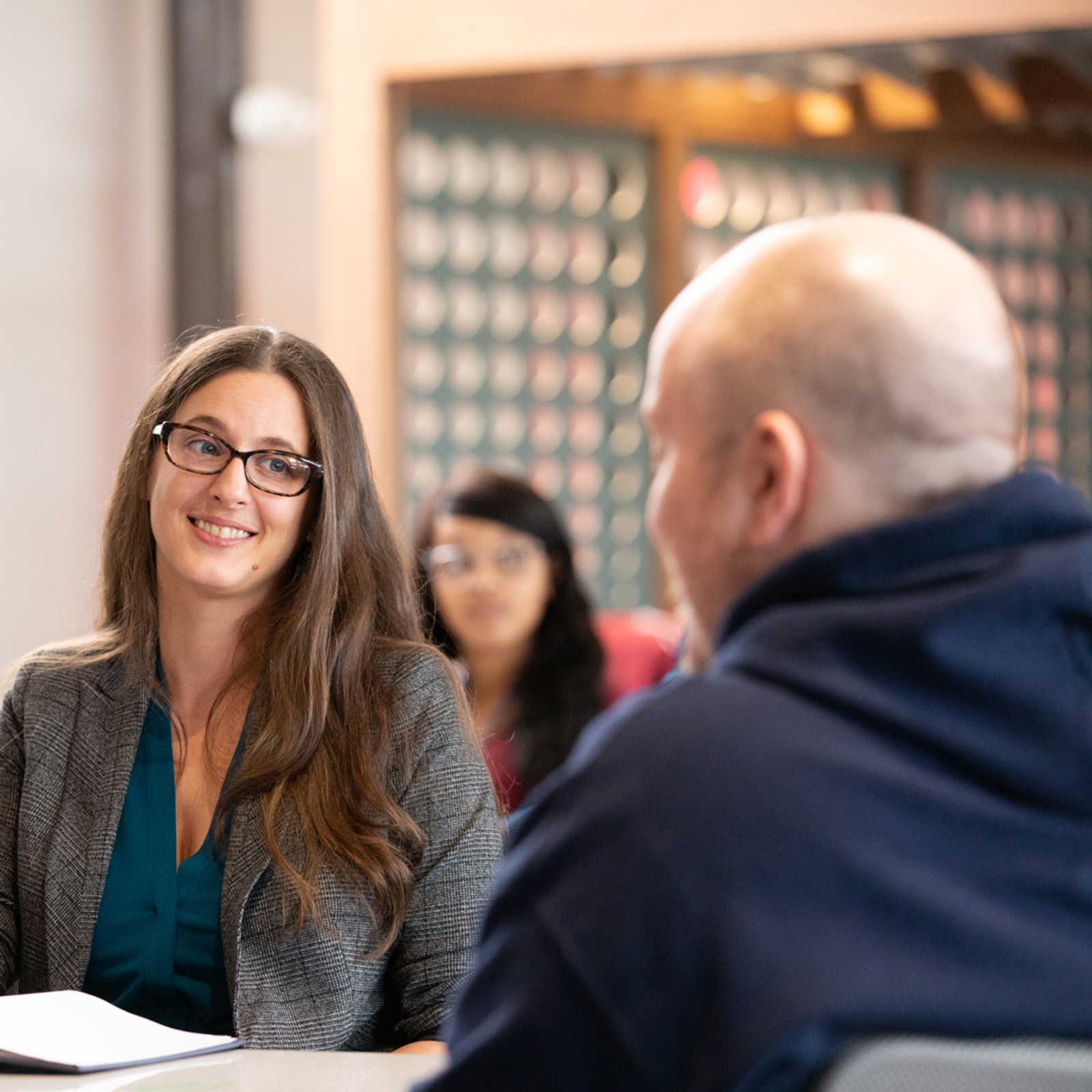 a woman sitting at a table with a man in the background