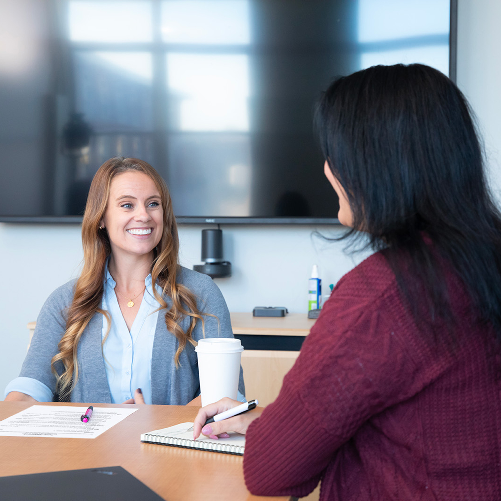 a woman sitting at a table with a cup of coffee and a woman smiling